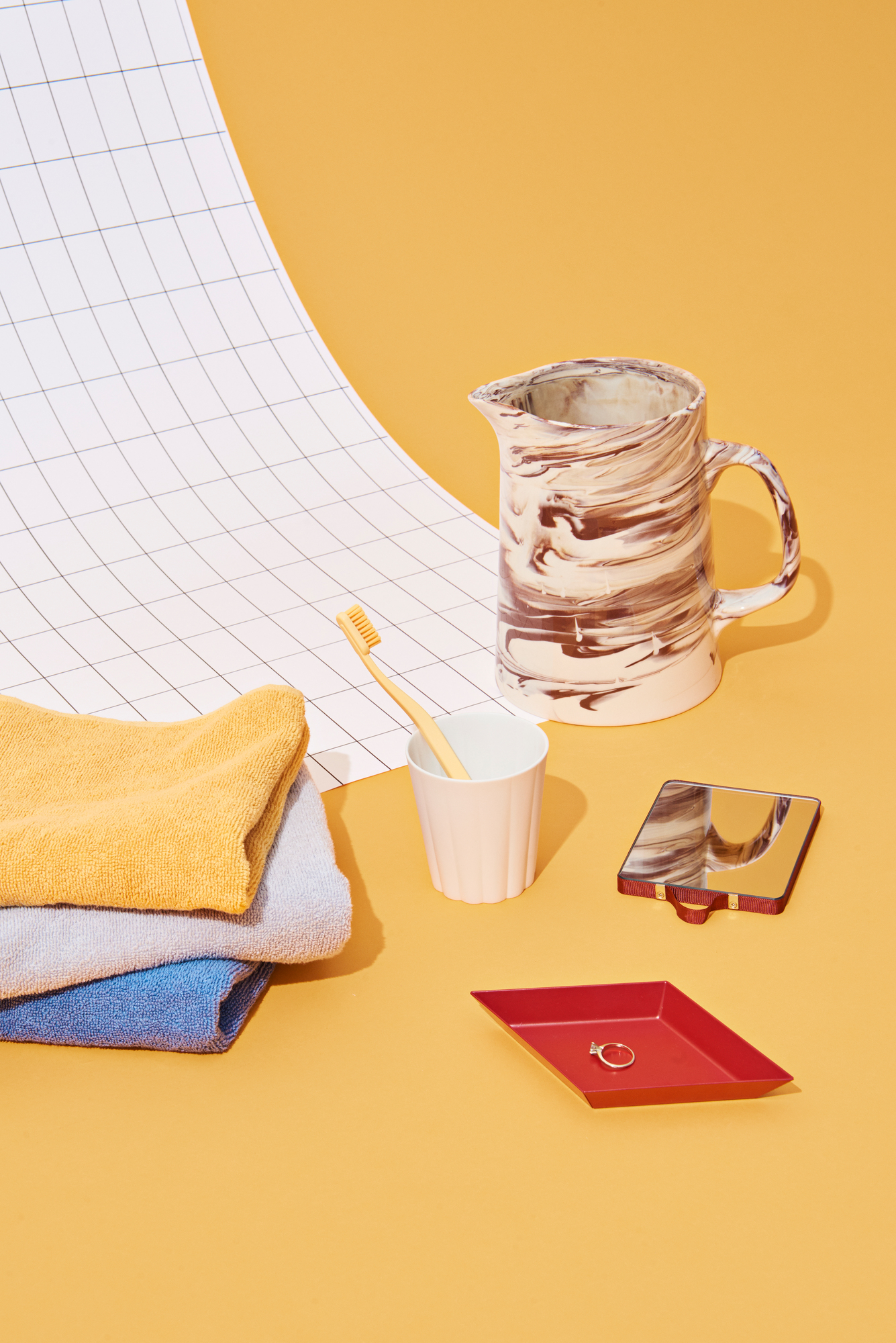 Produktfoto der Marbled Jug Karaffe von Hay, braun-weiß marmoriert, neben Badaccessoires auf gelbem Grund.