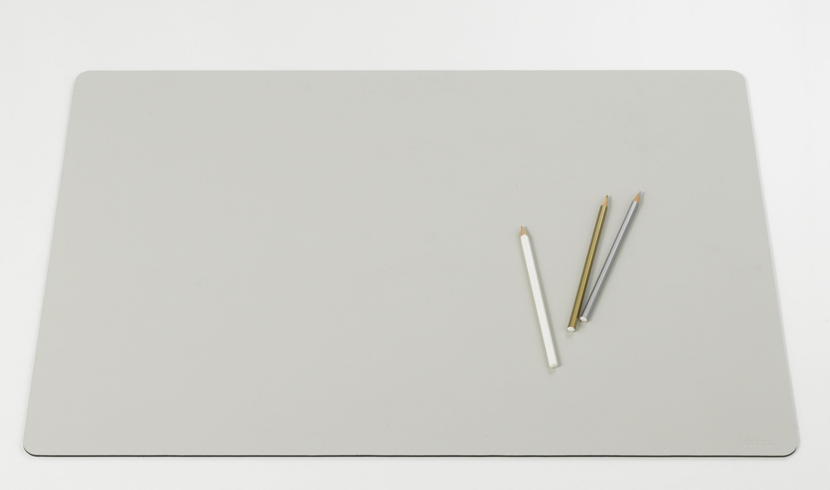 Graue Vitra Schreibtischunterlage Repad auf weißem Hintergrund mit drei Stiften. Büroaccessoire für den Schreibtisch.