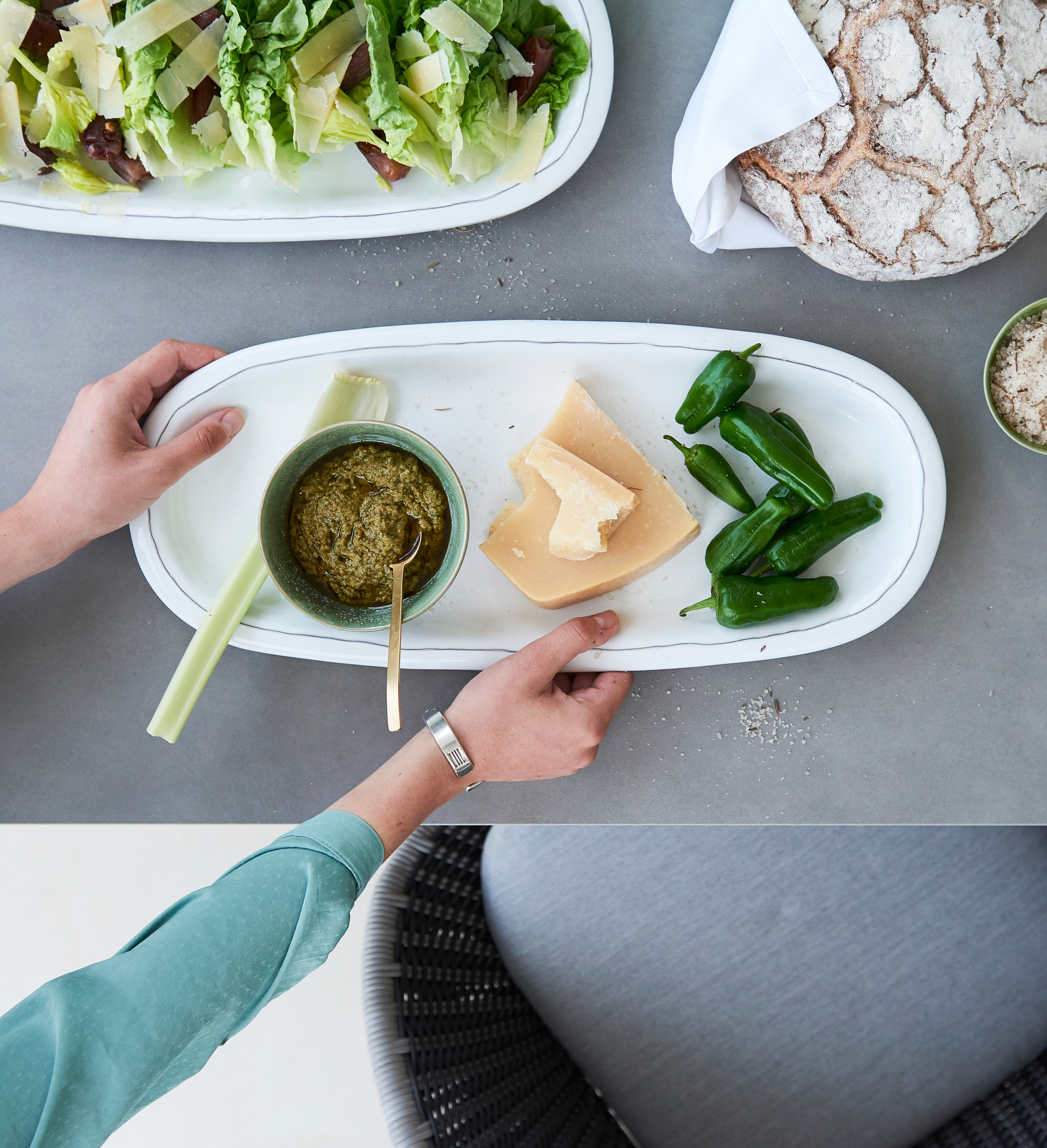 Pure Outdoor Esstisch: Detailaufnahme mit Speisen wie Salat, Pesto, Käse und Brot auf grauem Tisch.