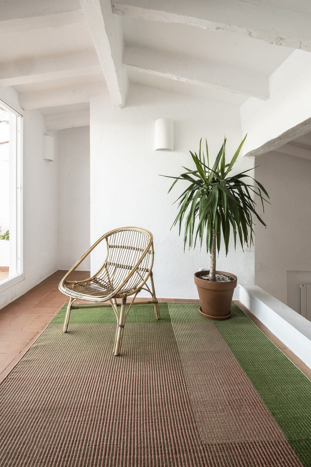 Nanimarquina Haze Rug Teppich in Braun und Grün mit Rattan-Stuhl und Zimmerpflanze in hellem Raum.