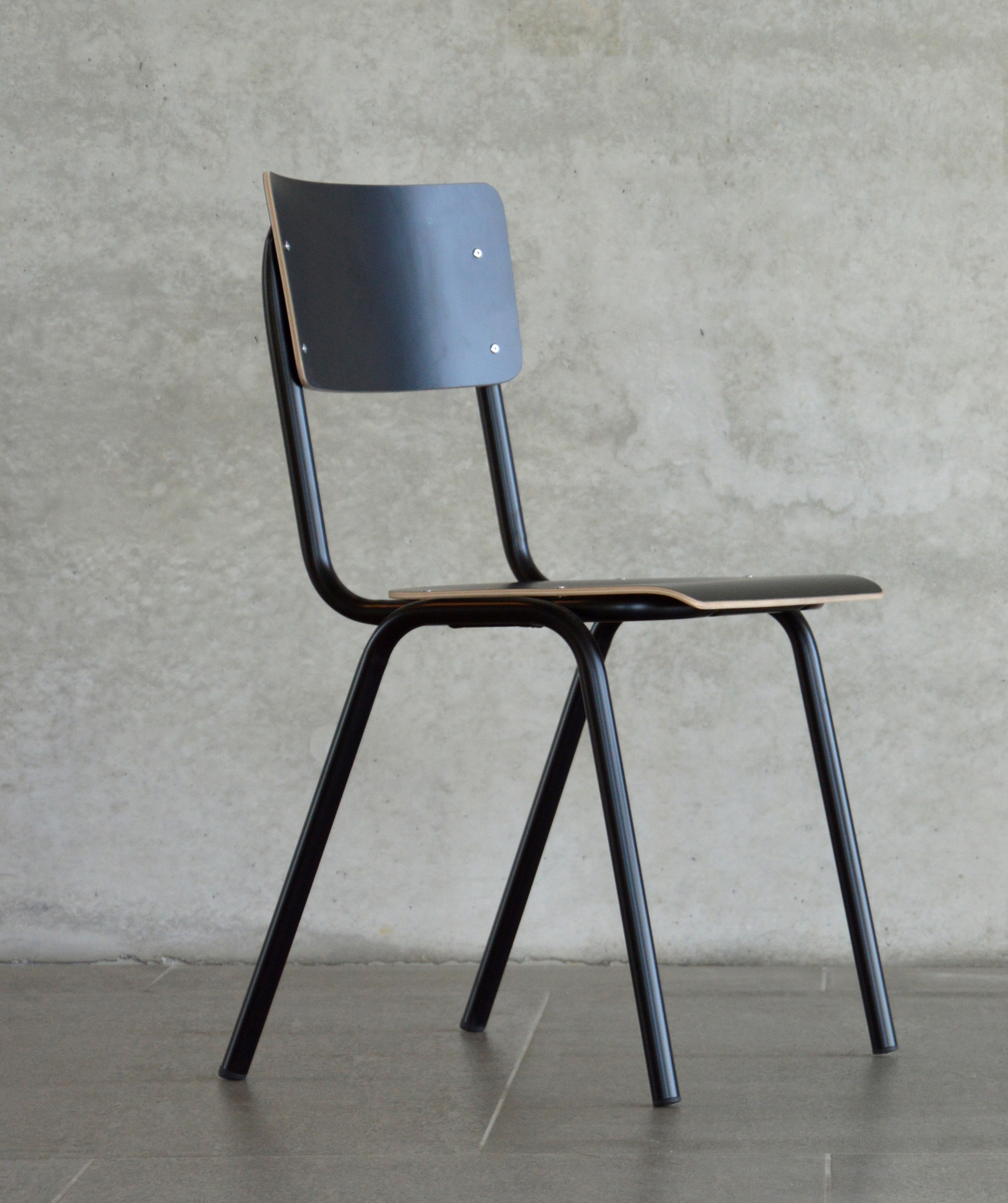 Schwarzer Jan Kurtz Zero Stuhl mit Stahlgestell und Holz Sitzfläche vor einer Betonwand.