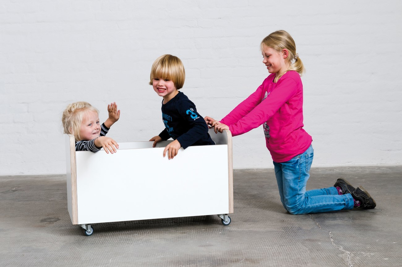 Kinder spielen mit der Growing Table Rollbox Truhe: Mädchen schiebt, Jungen sitzen in der Spielzeugkiste.