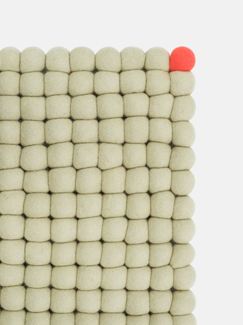 Detailansicht des grünbeigen Filzteppichs "Big One" mit Filzkugeln und einer roten Filzkugel.