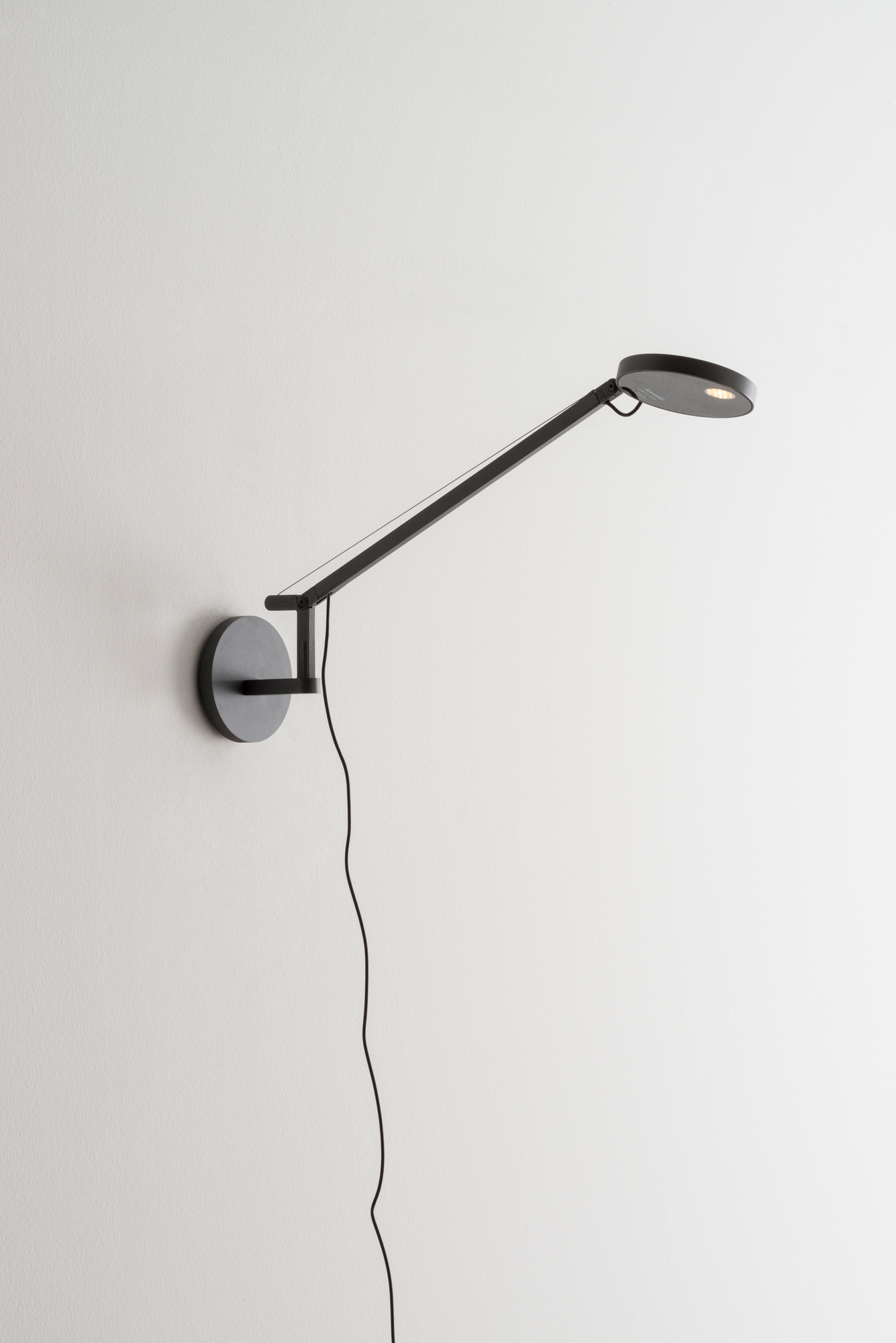 Schwarze Demetra Micro Wandleuchte von Artemide mit verstellbarem Arm und warmweißem Licht (2700K).