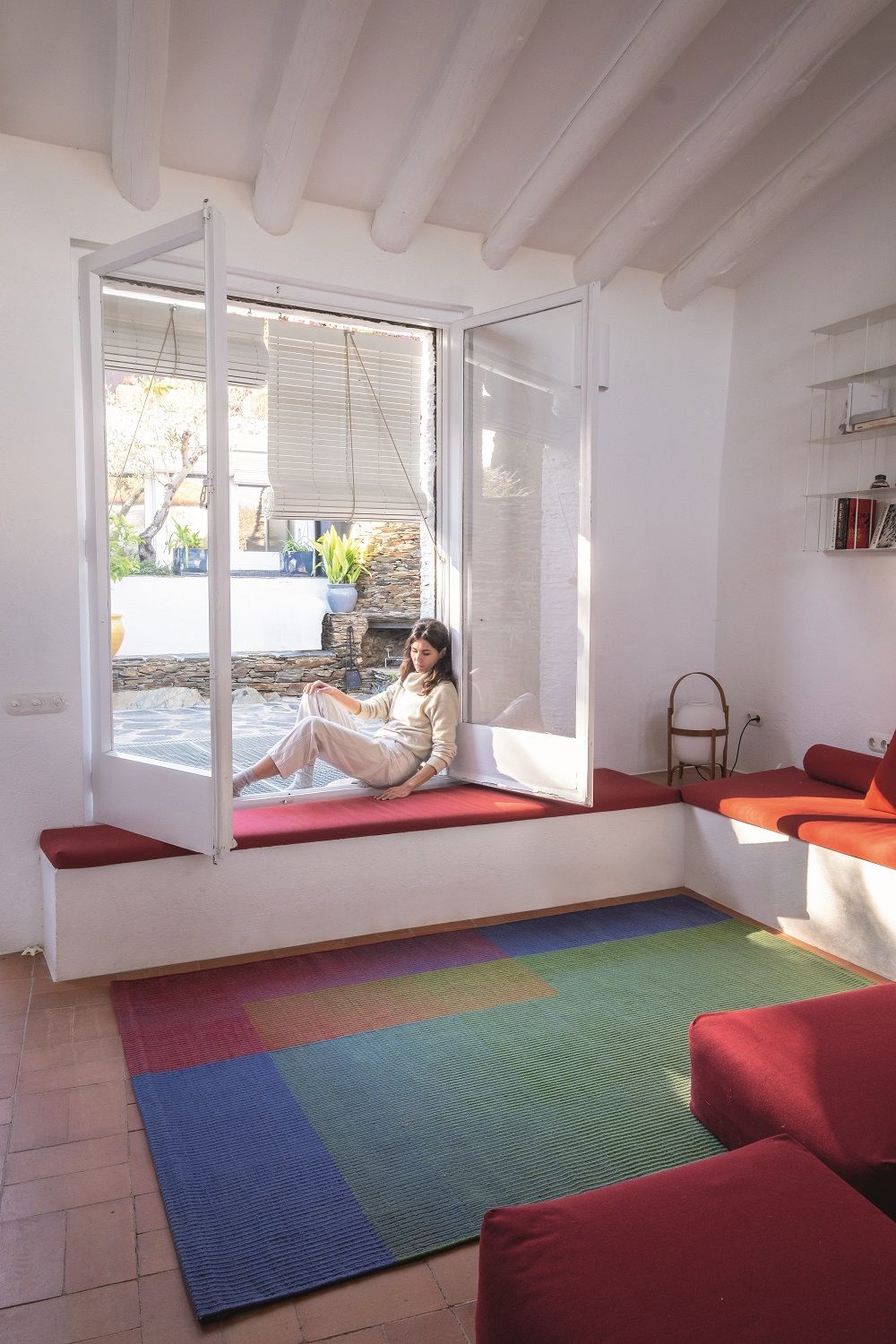 Frau sitzt am Fenster, im Vordergrund der bunte Haze Rug Teppich von Nanimarquina.