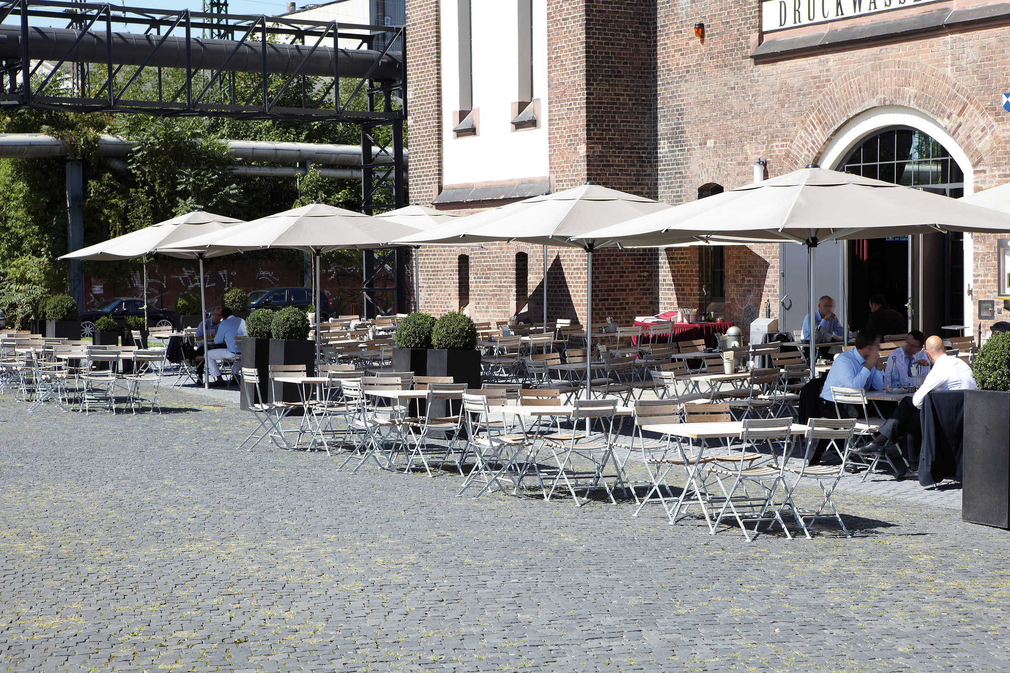 Außenbereich mit vielen Lucca Klapptischen in Natur von Jan Kurtz, ideal für Gastronomie.