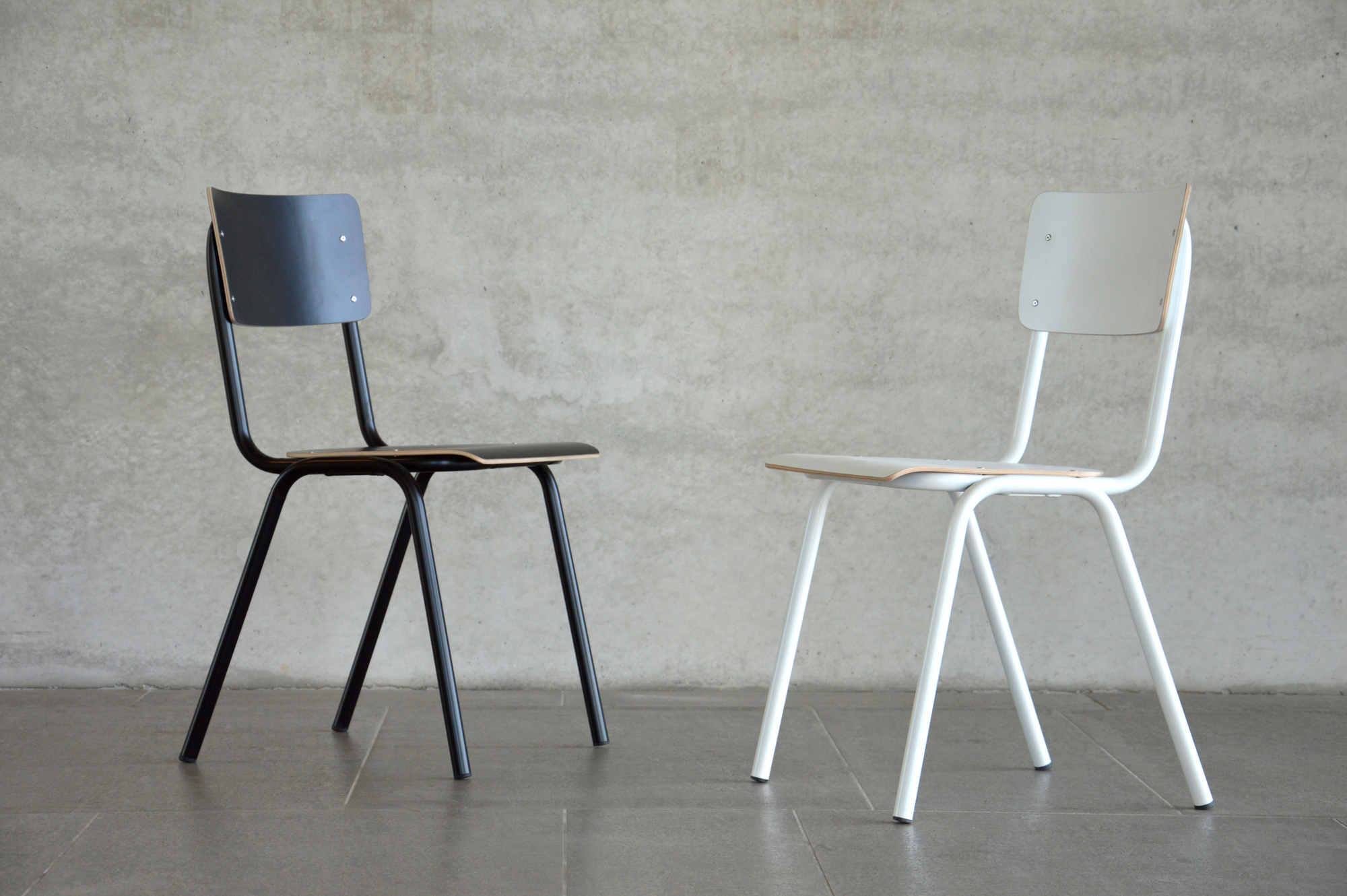 Zwei Jan Kurtz Zero Stühle, einer schwarz, einer weiß, vor einer Betonwand.