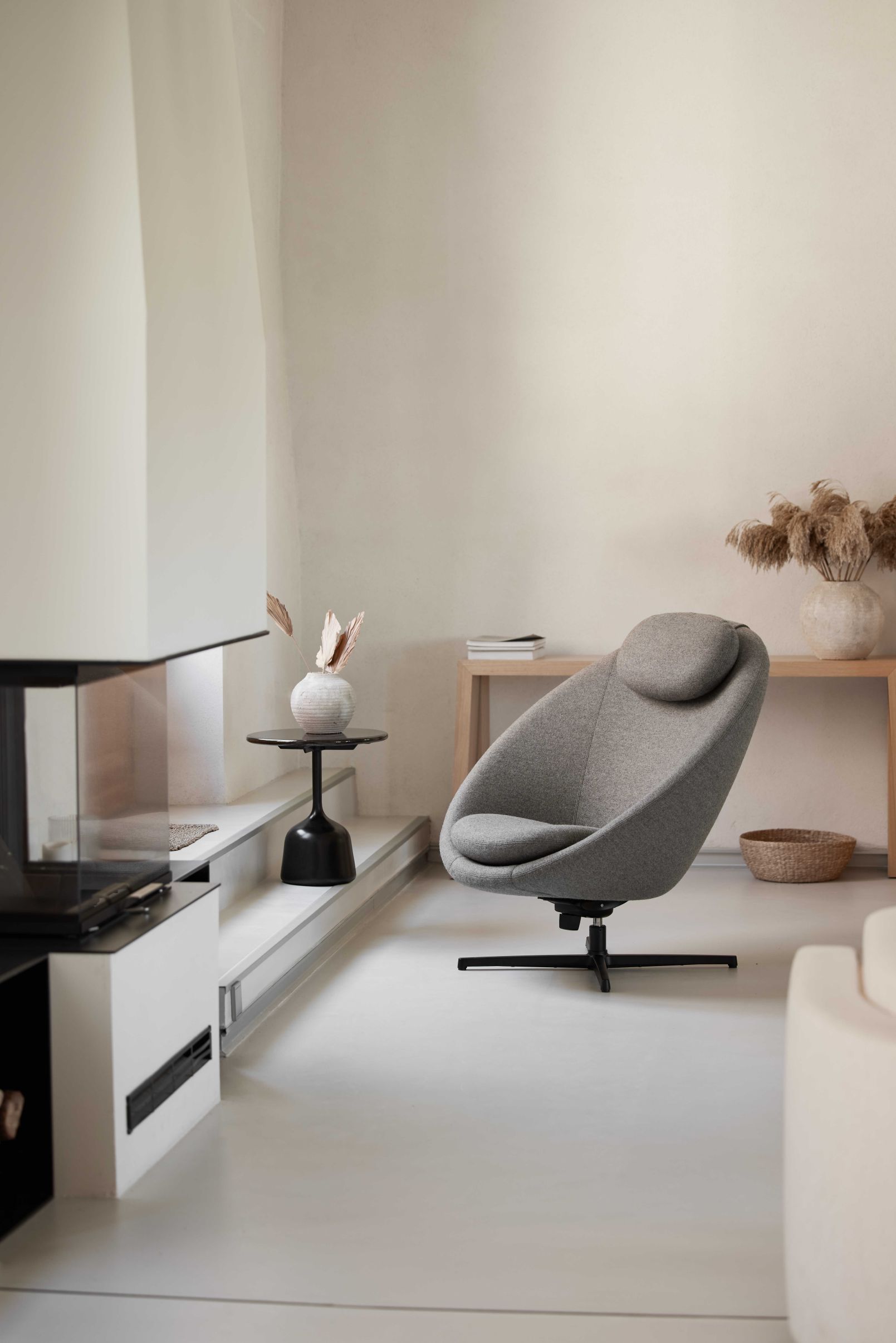 Grauer Cane-Line Pace Loungesessel mit Kopfstütze und schwarzem Drehfuß in modernem Wohnzimmer.