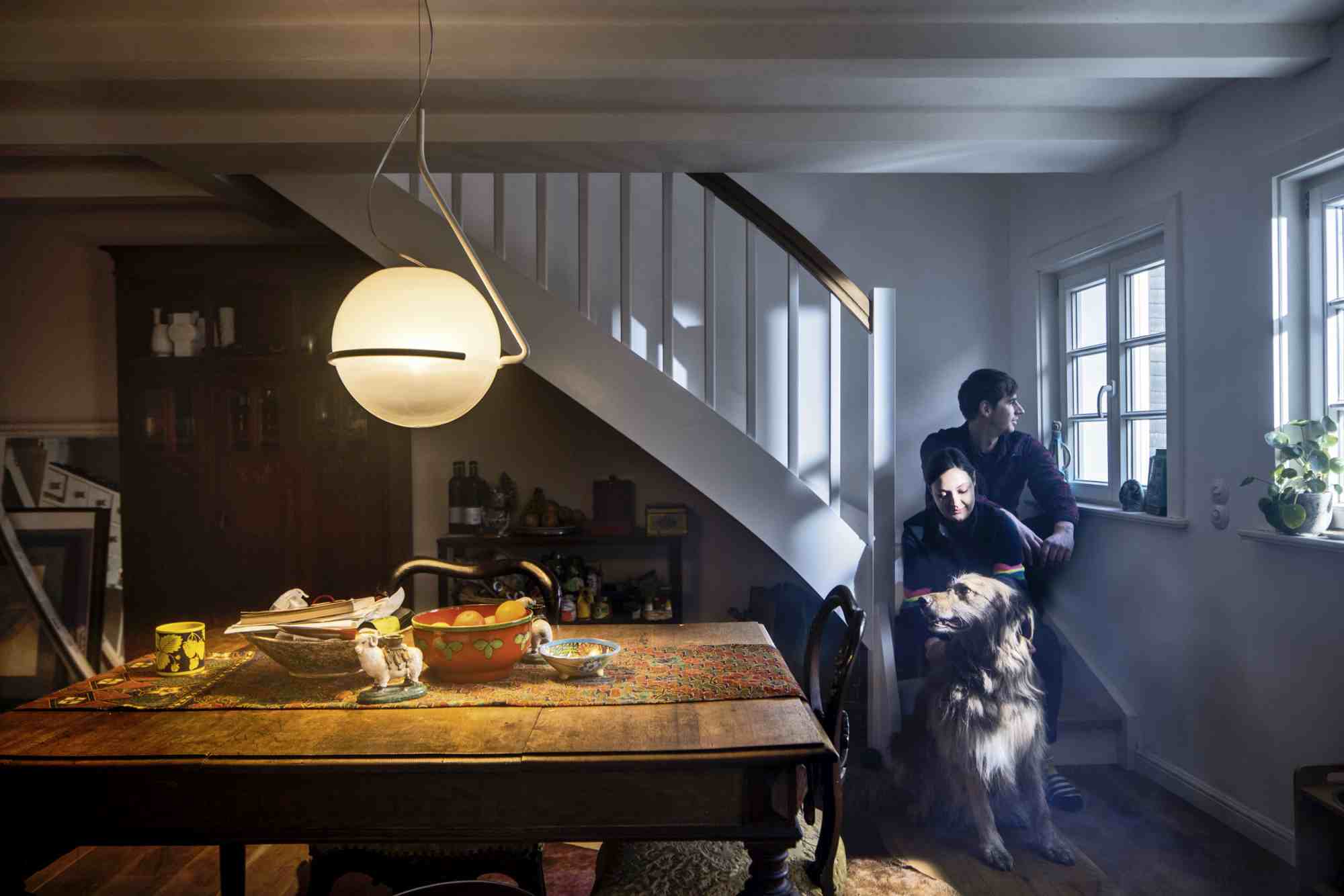 Tonda Pendelleuchte von Foscarini über Esstisch in gemütlichem Wohnzimmer mit Paar und Hund.