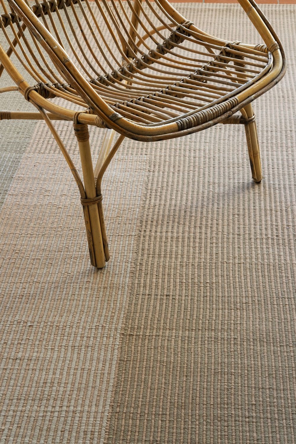 Detailaufnahme des Nanimarquina Haze Rug Teppichs mit feinen, vertikalen Streifen und einem Rattan-Stuhl.