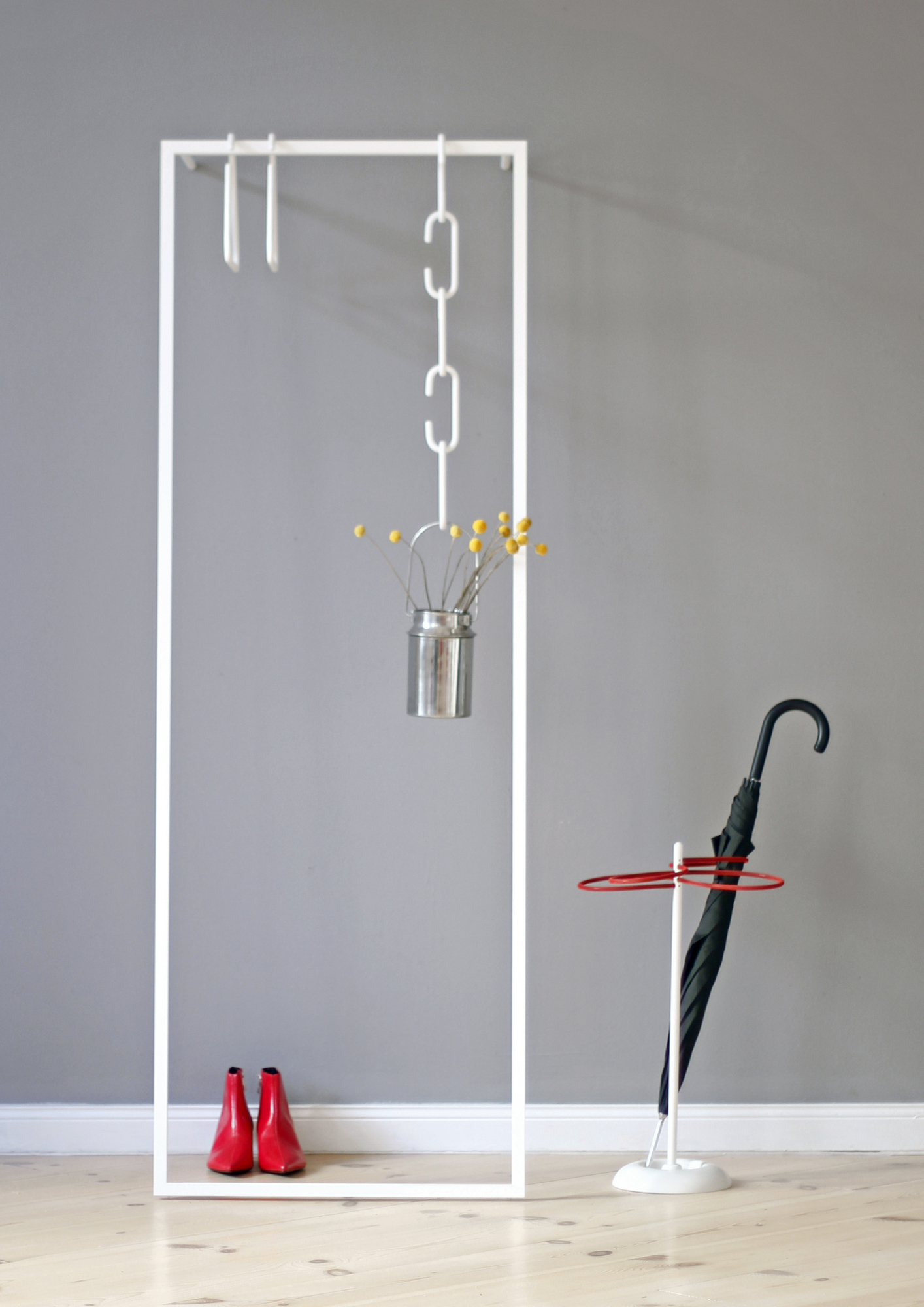 Weiße Leano Anlehngarderobe von Roomsafari mit roten Schuhen, Regenschirm und Dekoration vor grauer Wand.