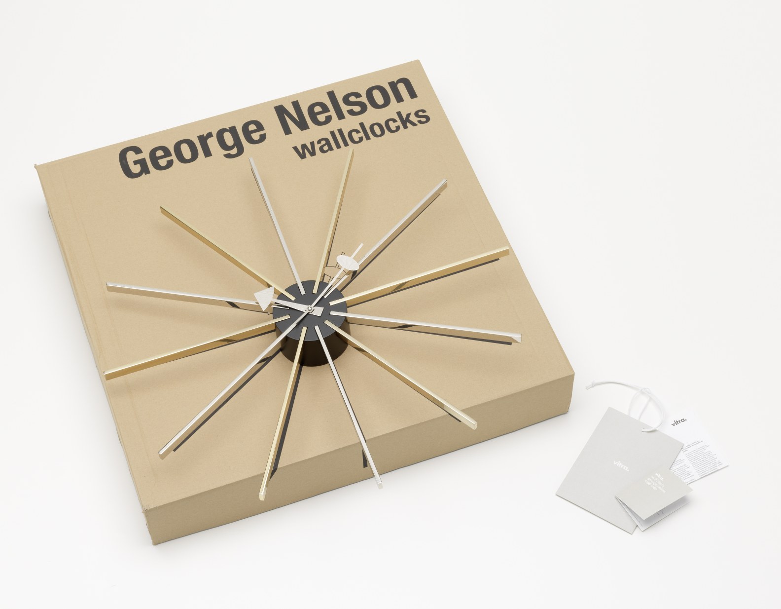 Star Clock Wanduhr von Vitra auf Karton, goldene und silberne Strahlen, modernes Design.