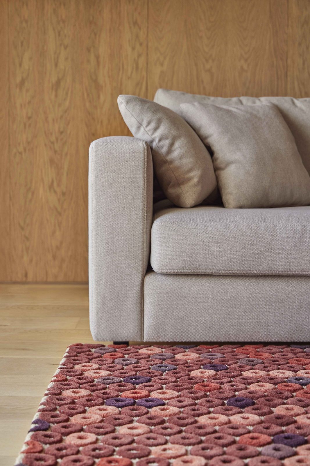 Detailaufnahme des Chimos Rug Teppich Gan mit Muster aus roten und violetten Kreisen vor Sofa.