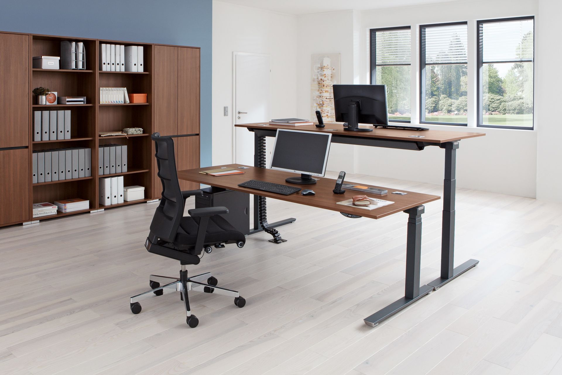 Palmberg Crew Sitz-Stehtisch mit brauner Tischplatte und schwarzem Gestell im modernen Büro. Ergonomischer Arbeitsplatz.