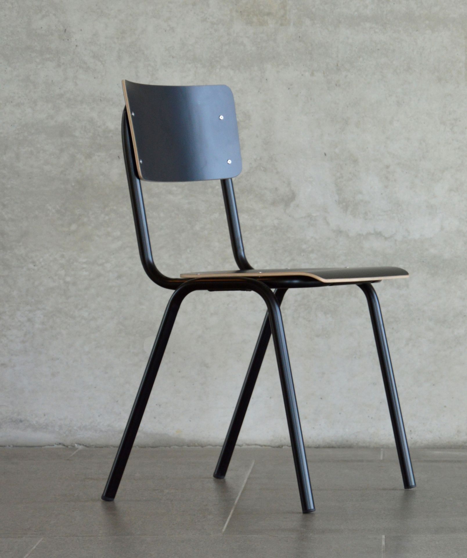Schwarzer Jan Kurtz Zero Stuhl mit Stahlgestell und Holz Sitzfläche vor einer Betonwand.