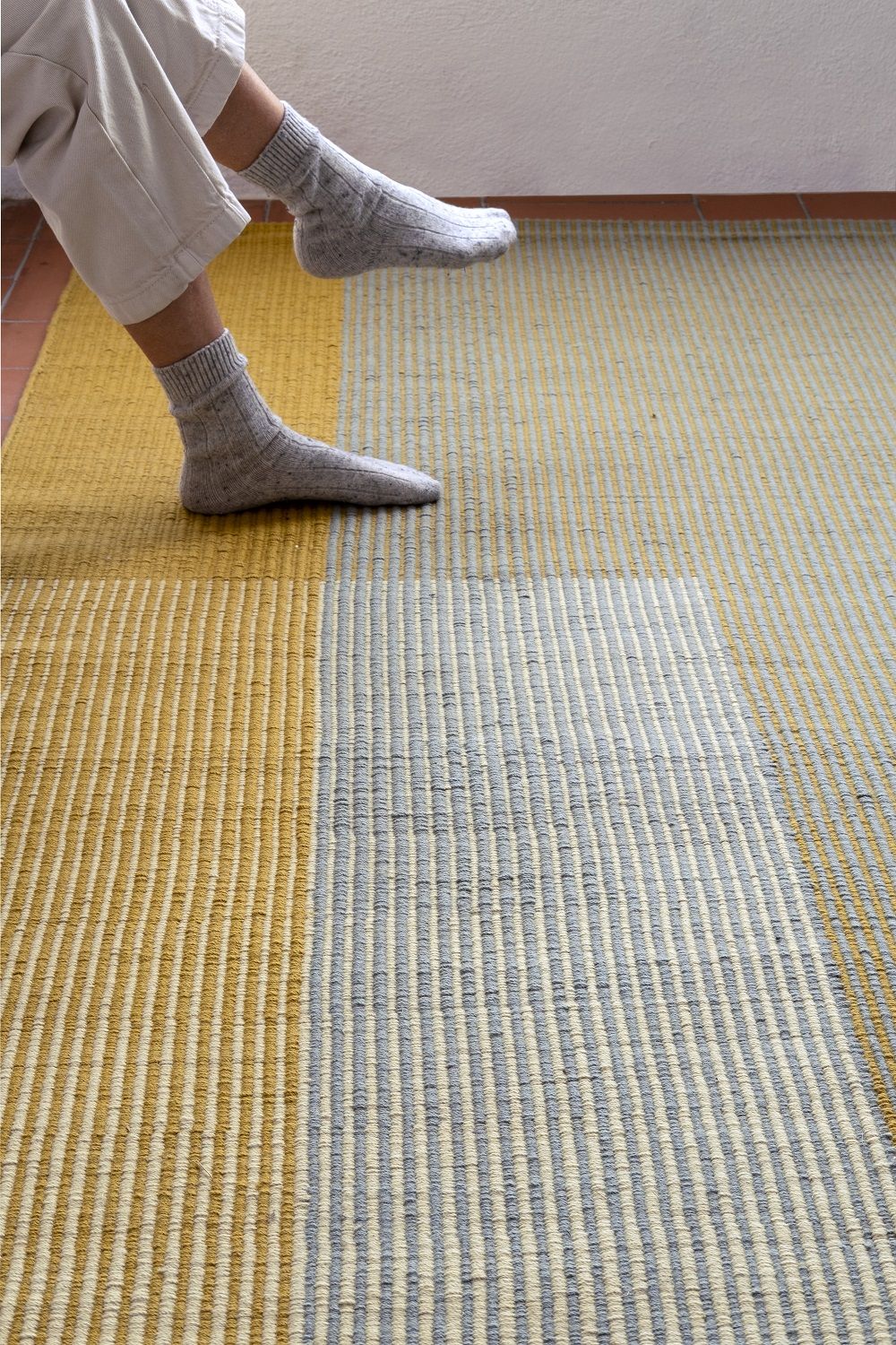 Detailaufnahme des Nanimarquina Haze Rug Teppichs in Gelb und Grau mit Wollsocken.