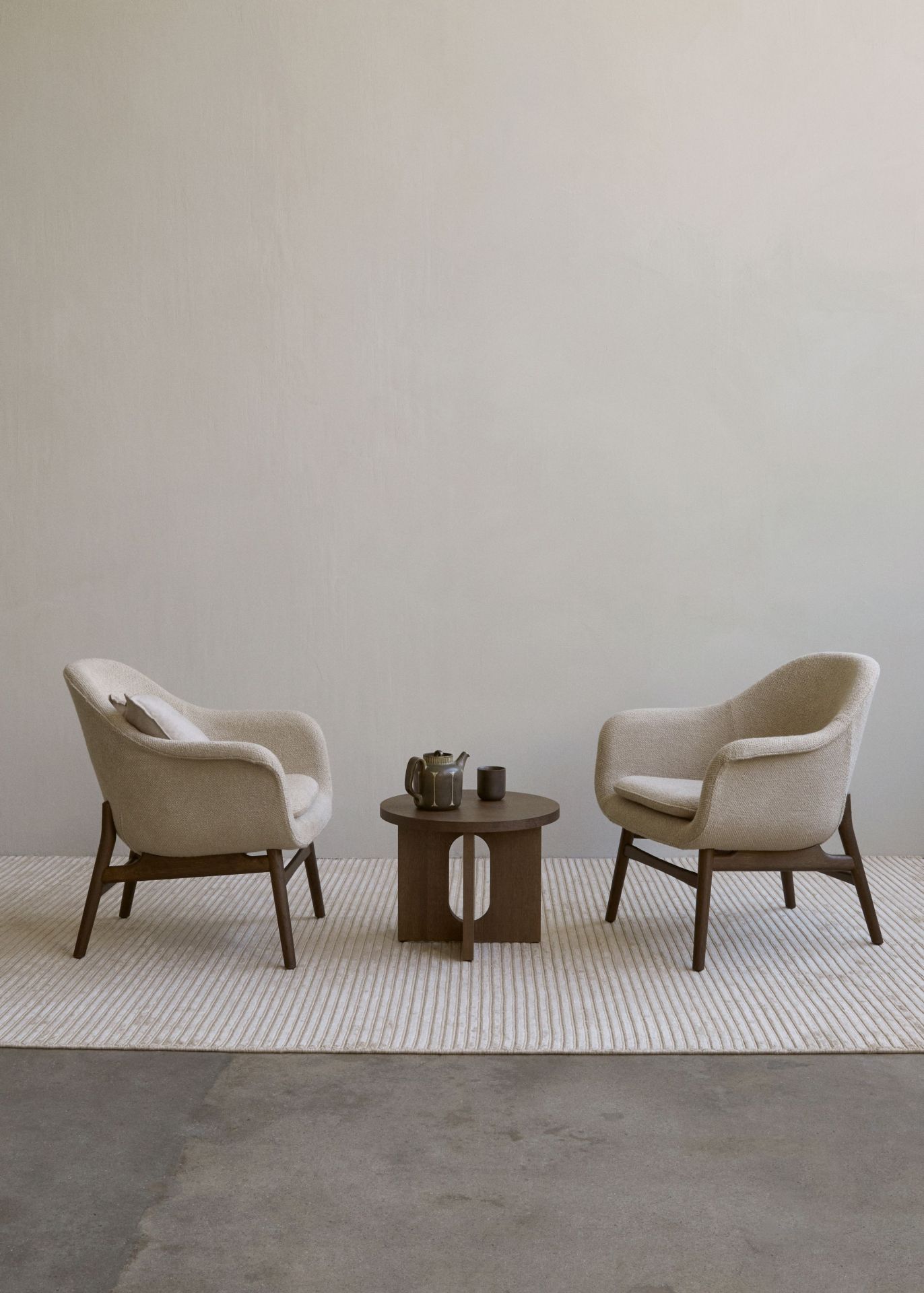 Androgyne table d'appoint Ø50 cm Audo Androgyne Beistelltisch aus Walnuss von Audo zwischen zwei Sesseln auf einem Teppich.