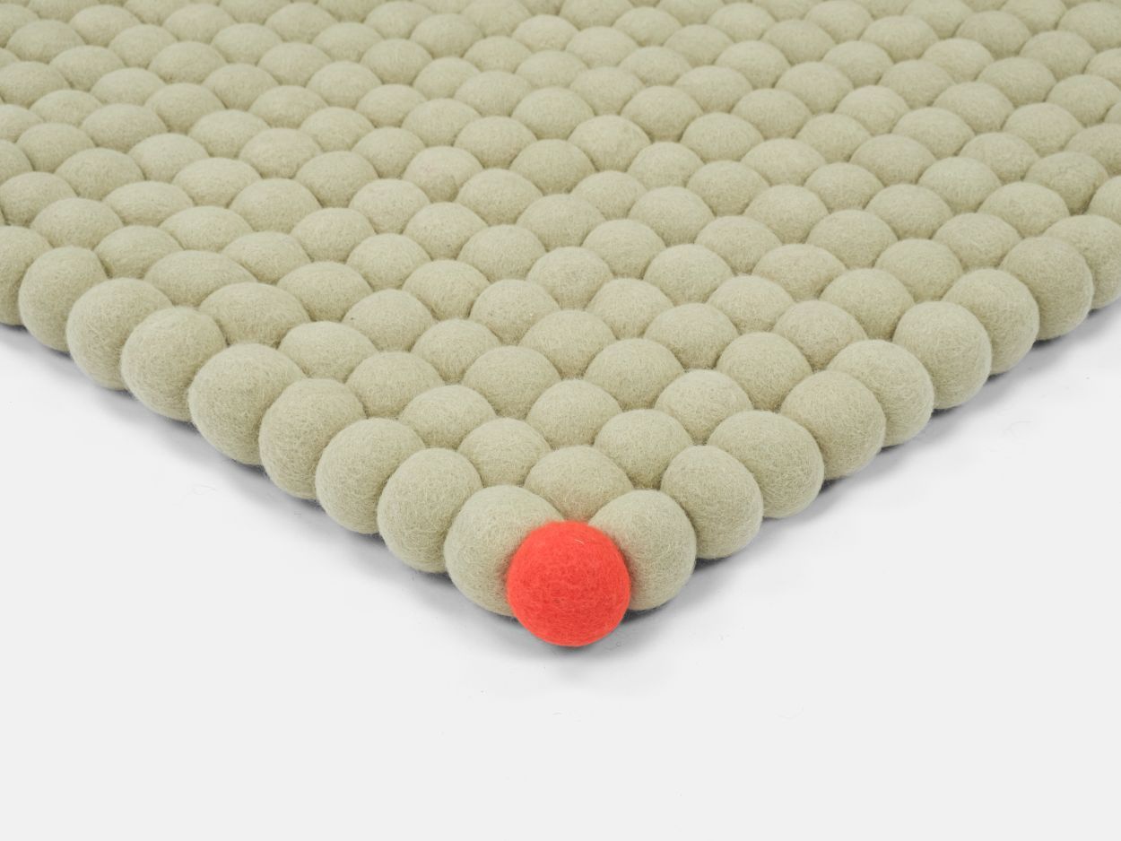 Detailaufnahme: Grünbeiger Filzteppich mit Filzkugeln, ein roter Akzent. Big One Teppich von myfelt.