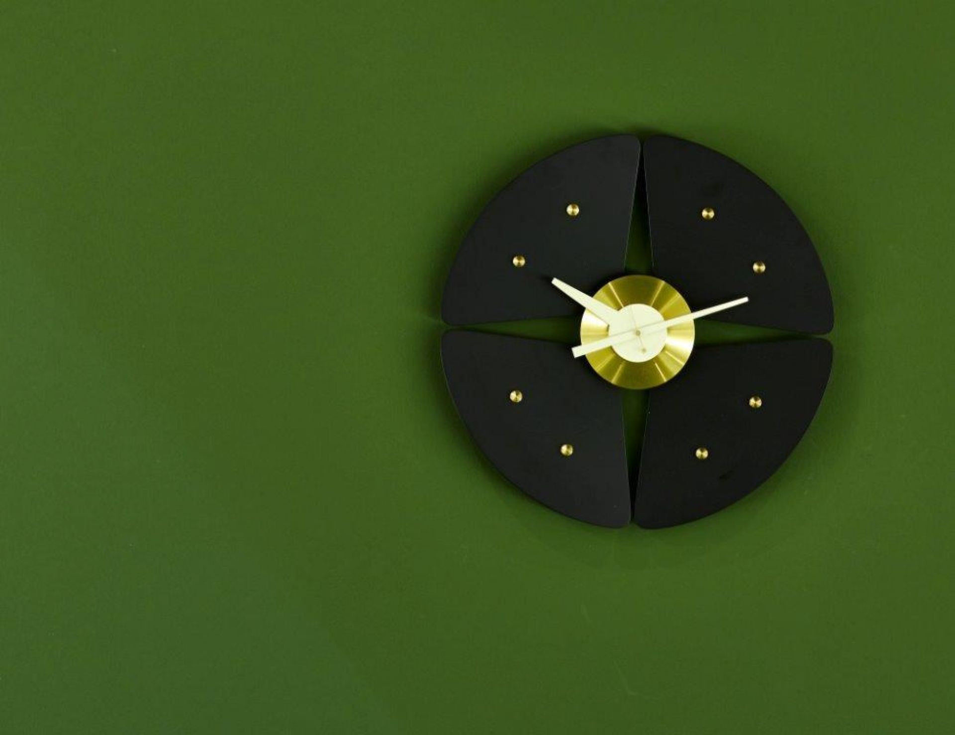 Schwarze Petal Clock Wanduhr von Vitra mit goldenen Akzenten vor einem grünen Hintergrund.