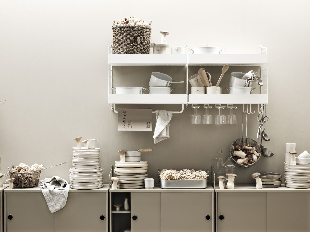 Detailaufnahme eines weißen String Furniture Regals mit Metallboden (58cm) und Küchenutensilien.