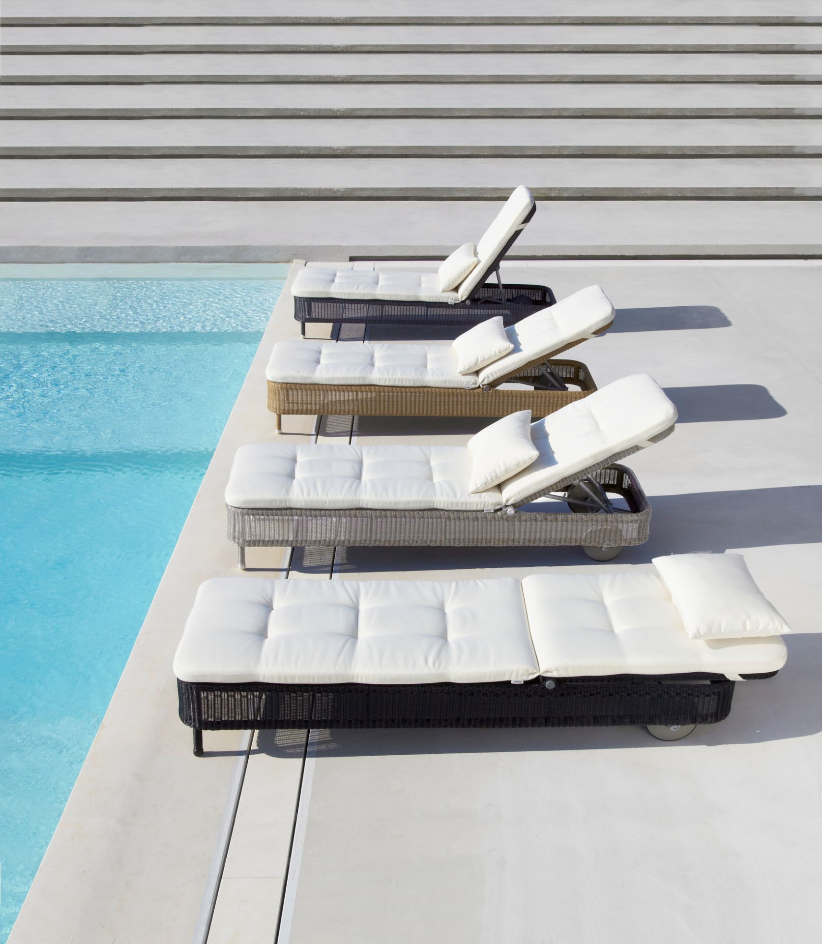 Mehrere Cane-Line Sonnenliegen mit weißem Presley Outdoor Kissensatz in Taupe am Pool.