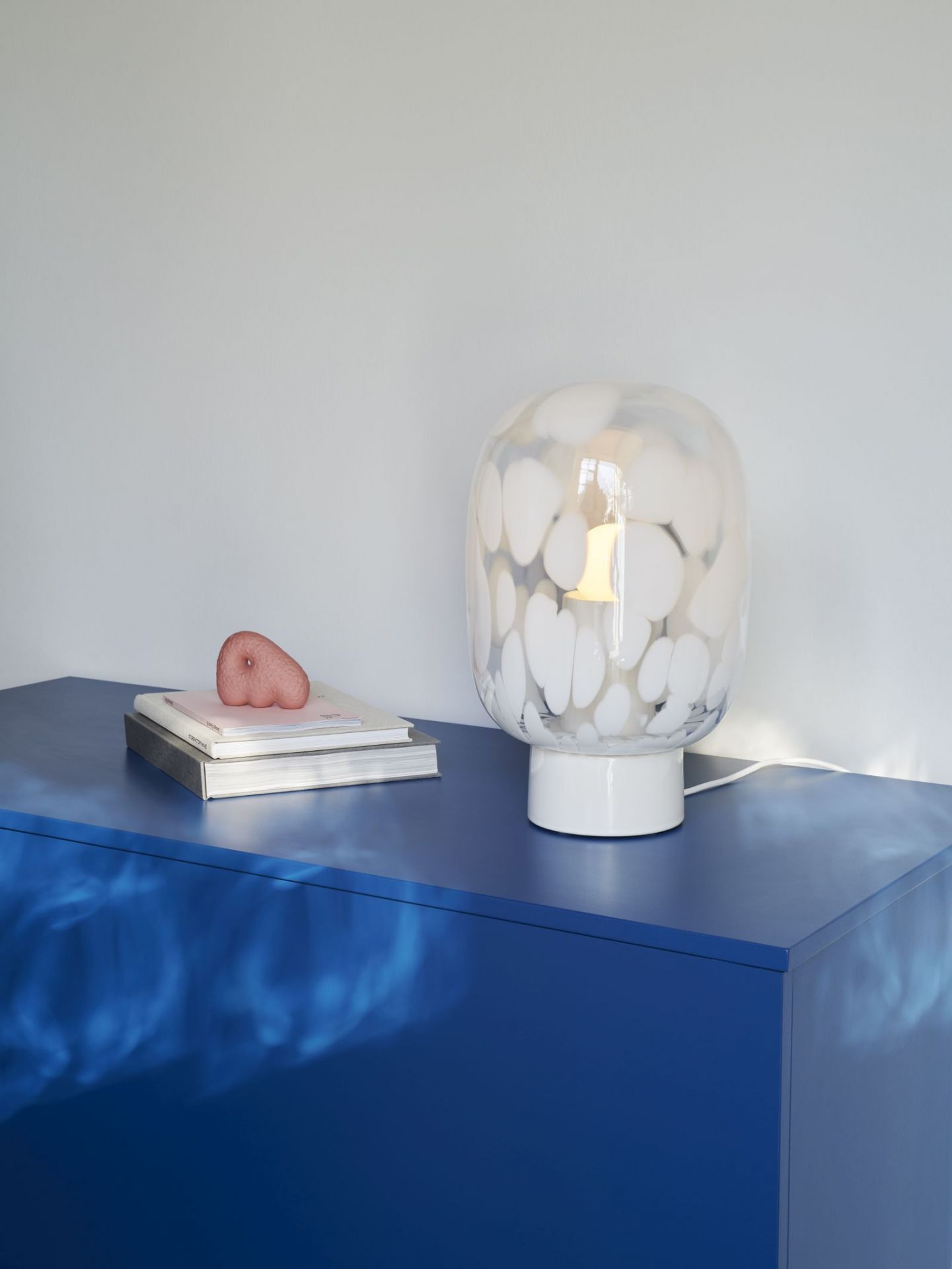 Weiße Flakes Tischleuchte mit Kristallglas auf blauem Schrank, moderne Wohnraumbeleuchtung.