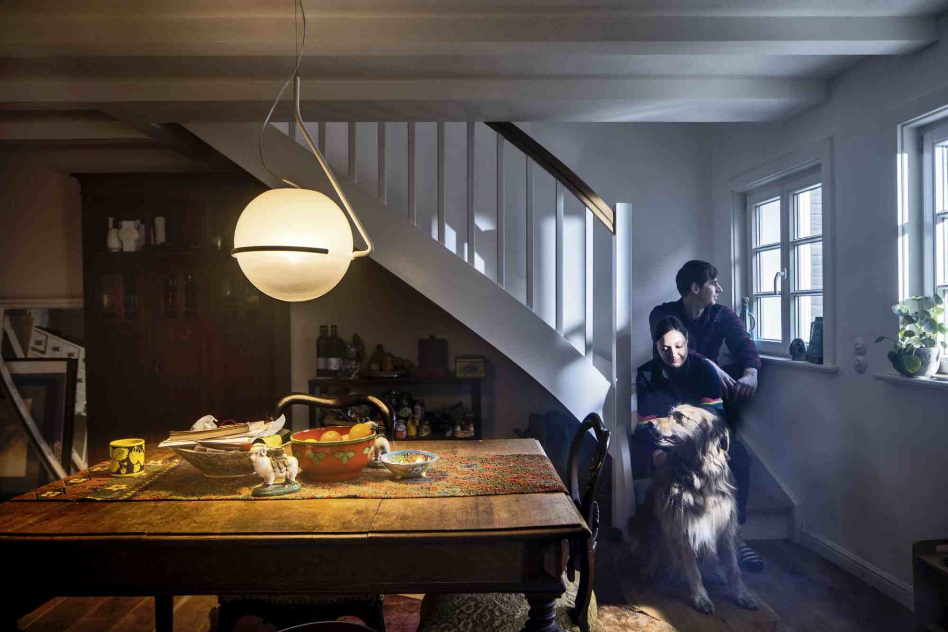 Tonda Pendelleuchte von Foscarini über Esstisch in gemütlichem Wohnzimmer mit Paar und Hund.