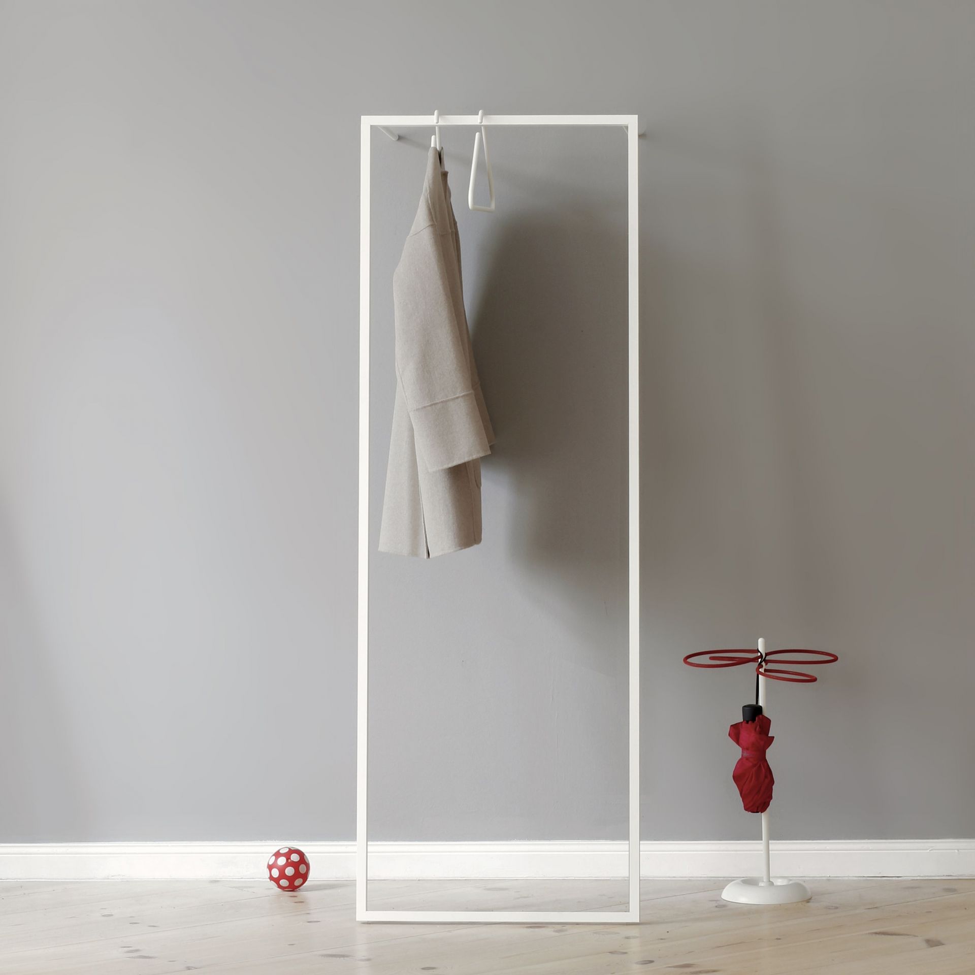 Weiße Leano S Anlehngarderobe von Roomsafari mit Mantel, Schirmständer und Ball vor grauer Wand.