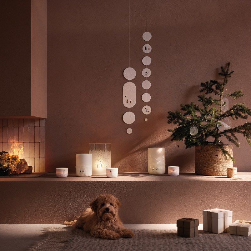 Winterliche Dekoration mit Poesie Windlicht, Schneelandschaft-Motiven, kleinem Weihnachtsbaum, Geschenken und Hund vor Kamin.