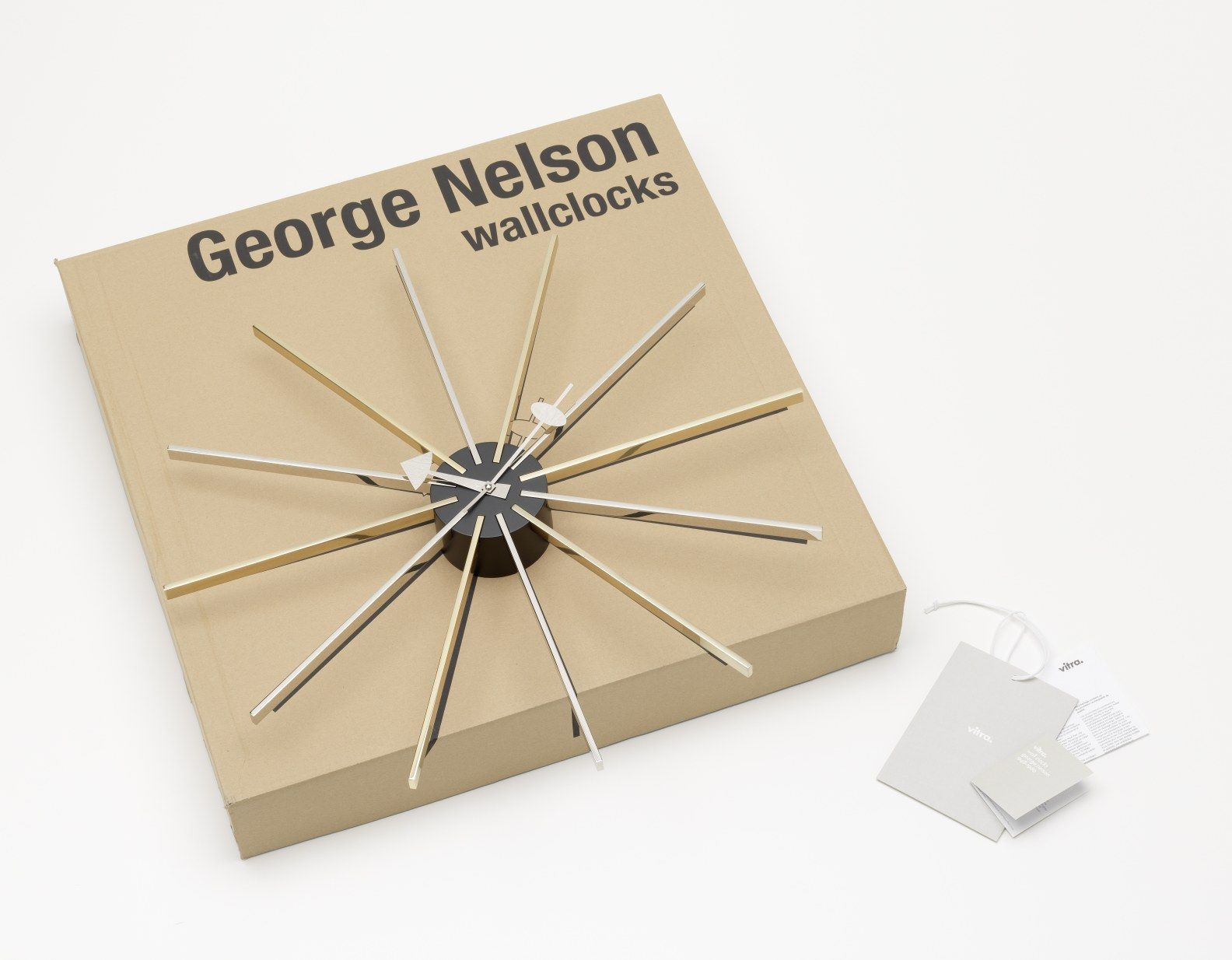 Star Clock Wanduhr von Vitra auf Karton, goldene und silberne Strahlen, modernes Design.