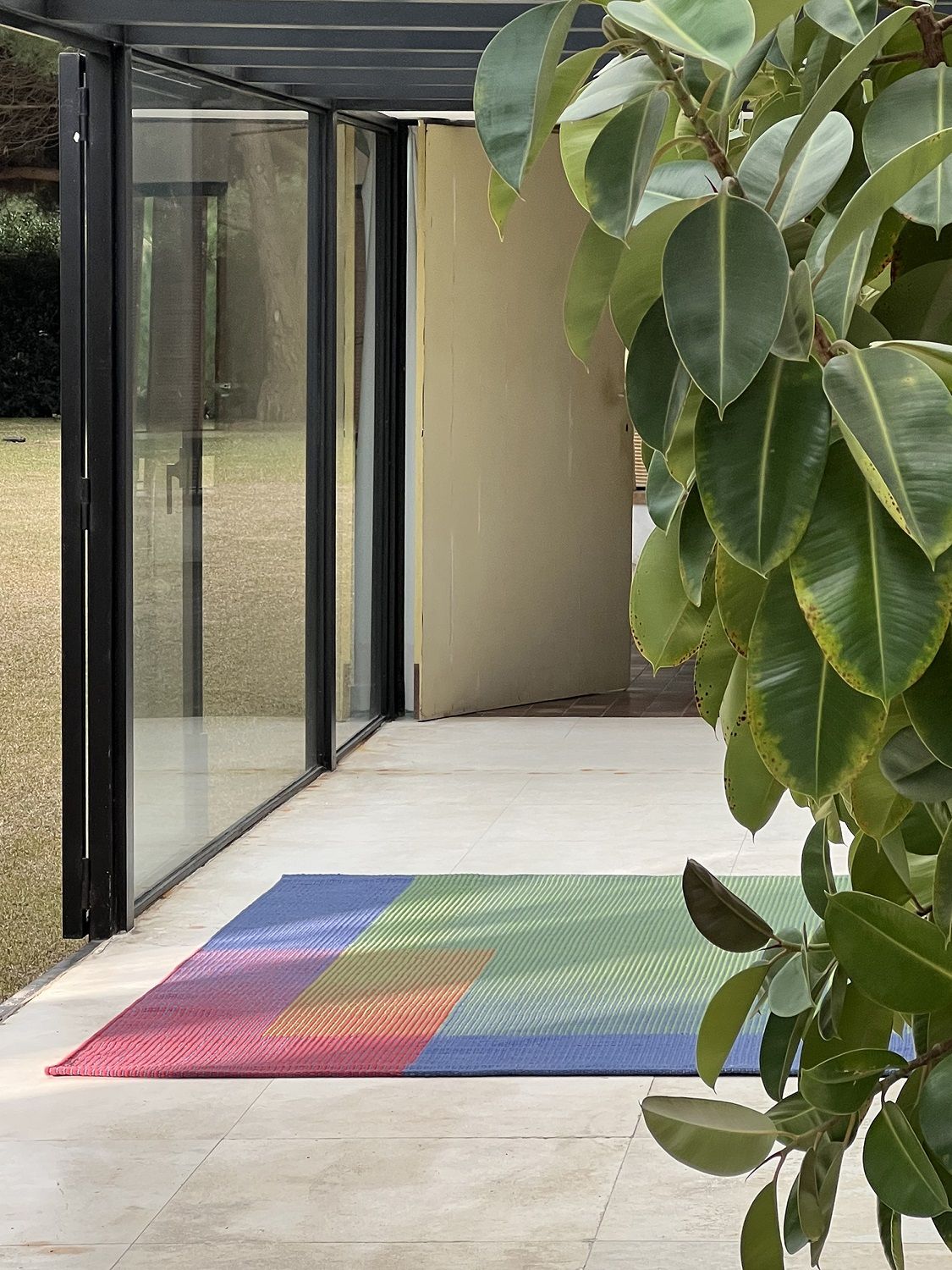 Nanimarquina Haze Rug Teppich mit Farbverlauf in Rot, Blau und Grün auf einer Terrasse.