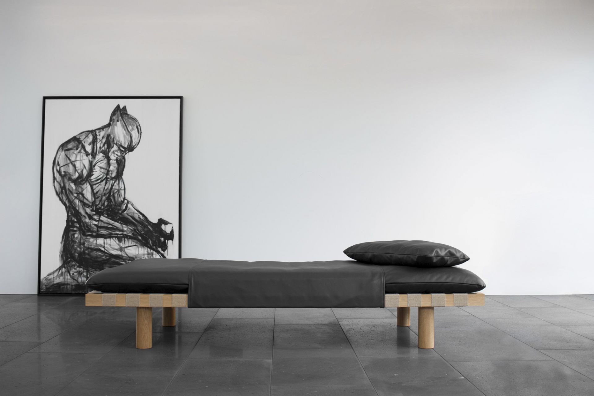 Schwarzes Pallet Daybed mit Lederbezug und Kissen vor weißer Wand und Kunstwerk.
